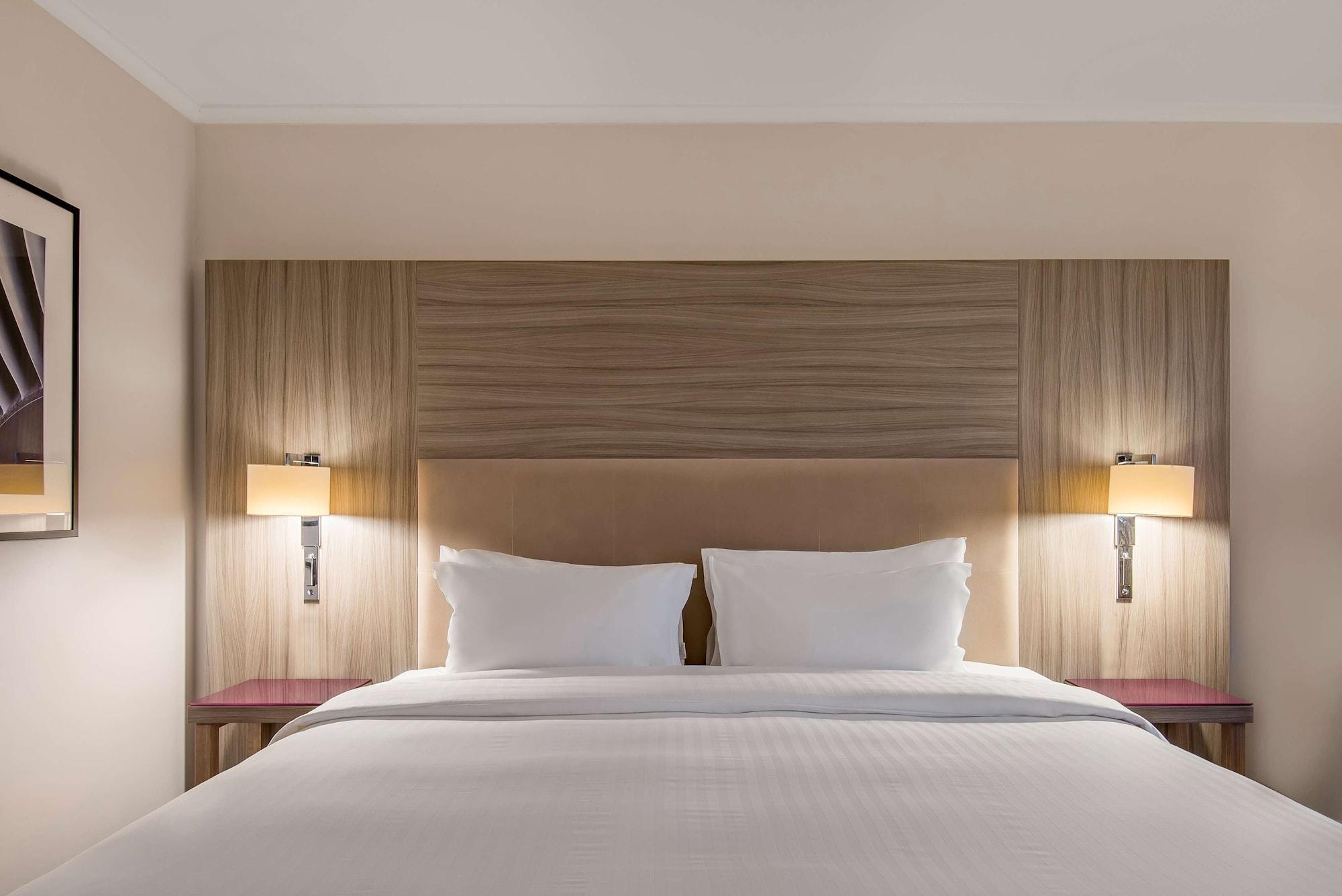 Radisson Blu Manchester Airport Hale  Esterno foto The photo shows a well-decorated hotel room featuring a large bed with two white pillows against a light-colored wooden headboard. On either side of the bed, there are stylish wall-mounted lights providing ambient lighting. The walls have a neutral t